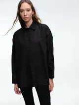 Camisa de corte holgado y líneas clásicas, confeccionada en algodón. Presenta cuello camisero, cierre frontal mediante botones y detalle de botones en los laterales para ajustar la silueta.