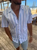 Camisa de manga corta con cuello cubano, confeccionada en algodón con diseño de rayas verticales en tonos blanco y celeste.