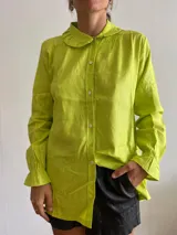 Camisa verde lima de lino con cuello babero, mangas largas con puños fruncidos y cierre frontal con botones. 