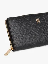 Billetera grande color negro con cierre perimetral dorado. El exterior presenta un patrón texturizado de monogramas en relieve y un logo metálico central.