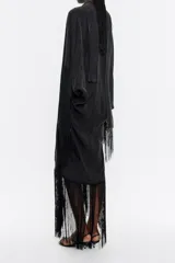 Vestido largo negro de lyocell con corte oversize, escote en V pronunciado, manga corta murciélago con maxiflecos, pieza extraíble para el cuello con flecos y bajo con maxiflecos.