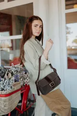 Mini cartera de cuero gamuzado en color marrón oscuro, con solapa frontal, cierre de hebilla metálica y correa ajustable al hombro.