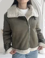 Chaqueta verde militar de gamuza sintética con interior de piel sintética color crema. Tiene cierre frontal con cremallera, cuello con solapas grandes y cinturón con hebilla en los puños.