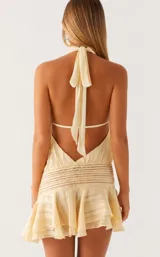 Vestido corto de satén color crema con diseño de rayas verticales sutiles. Presenta cuello alto tipo halter, cintura elástica fruncida y falda con volados en el ruedo.