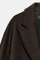 Abrigo largo de Zara confeccionado en hilatura con lana, de color marrón oscuro. Cuenta con cuello solapa, manga larga, bolsillos de vivo en el delantero y cierre frontal con dos botones.