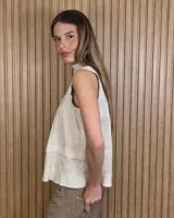 Musculosa marrón sin mangas, con cuello alto, escote en V y detalles de pespuntes blancos en contraste. Presenta pliegues y alforzas frontales.