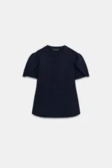 Chaqueta entallada azul marino de punto, con cuello redondo y mangas cortas abullonadas con aberturas. Cierre frontal con botones forrados a tono.