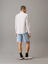 Camisa de manga larga Calvin Klein confeccionada en popelina de algodón elástico con diseño de rayas verticales. Presenta cuello en punta, cierre frontal de botones, bolsillo de parche en el pecho y bajo redondeado.