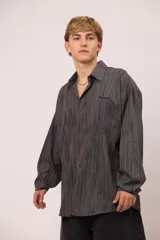 Camisa de manga larga con corte relajado, confeccionada en microfibra con estampado abstracto de líneas verticales en tonos grises. Presenta cuello clásico, cierre frontal con botones, bolsillo en el pecho con el nombre de la marca bordado.