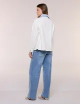 Campera de denim blanco de corte holgado con hombros caídos, cuello con solapa en contraste de color celeste, cierre frontal con botones metálicos y bolsillos delanteros con solapa.