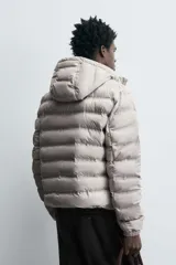 Campera puffer acolchada de corte regular fit en color negro, confeccionada en tejido técnico repelente al agua. Presenta cuello subido con capucha, cierre frontal de cremallera, mangas largas con puños elásticos y bolsillos laterales de vivo.