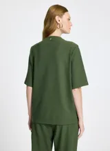Remera verde militar de tejido de punto con corte recto, cuello redondo y mangas cortas. Presenta bolsillos delanteros alargados con solapas y botones, bajo largo y acabado pespunteado.