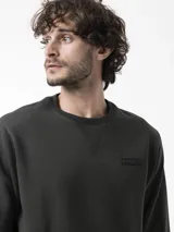 Buzo de cuello redondo verde oscuro, de manga larga, con detalle de costura en V en el cuello y pequeño parche engomado con la marca en el pecho.