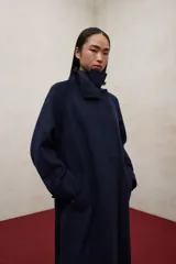 Abrigo largo de lana reciclada en color azul marino, con diseño de cuello alto, mangas raglán y cinturón ajustable a la cintura. Presenta un corte elegante y minimalista con cierre frontal oculto.