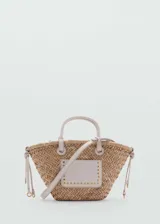 Bolso tipo cesta de fibra natural trenzada, con detalles en cuero sintético color crema. Incluye dos asas cortas de mano, una correa larga bandolera desmontable y un bolsillo frontal decorado con tachas metálicas doradas.