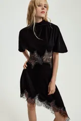Vestido midi de terciopelo negro con cuello redondo y pañuelo integrado en el mismo tejido. Presenta mangas cortas, aberturas laterales con detalle de encaje a tono y bajo asimétrico con terminación en encaje.