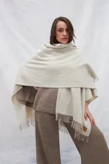 Ruana de lana 100% sin teñir en color tostado, con diseño de punto acanalado y terminación de flecos en el ruedo.