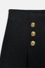 Pantalón de tiro alto con pierna ancha, confeccionado en sarga color tostado. Presenta detalle de doble hilera de botones metálicos dorados en el frente y pinzas verticales.