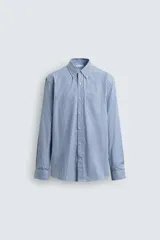 Camisa de corte regular fit confeccionada en tejido de algodón, con diseño de rayas verticales en tonos azules. Presenta cuello abotonado, manga larga con puños abotonados, cierre frontal de botones y un bolsillo en el pecho.
