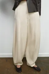Pantalón de tiro medio color beige claro, de pierna ancha y corte balloon. Presenta pliegues frontales y bolsillos delanteros ocultos en costura.