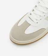 Championes de estilo casual, color blanco, con detalles en beige claro en los laterales y puntera de gamuza color gris claro. Posee suela de goma color caramelo y tirador trasero en color verde oscuro.