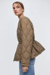 Campera acolchada marrón tipo puffer de nylon guateado, con diseño matelasseado de rombos, cuello redondo y cierre frontal. Cuenta con hombros caídos, mangas largas, bolsillos laterales discretos y cordón de ajuste en la cintura con tiras colgantes.