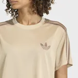 Remera Adidas Firebird de corte holgado, confeccionada en tejido tricot color beige. Presenta cuello redondo, mangas cortas con las icónicas tres rayas en color marrón y el logo del trébol bordado en el pecho.