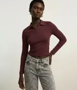 Blusa de manga larga confeccionada en tejido rib de algodón con cuello polo y escote en V. Presenta un diseño ajustado al cuerpo y acabado liso.