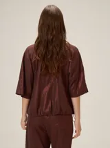 Chaqueta de lino y rayón color tostado, de corte holgado, mangas cortas amplias, cuello mao y cierre frontal oculto con cremallera. Presenta pespuntes a contratono en las costuras y cordón ajustable en el bajo.