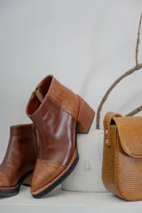 Botineta de cuero color suela, con diseño de punta fina y puntera texturizada con efecto reptil. Presenta una suela de madera clara con borde negro y cierre lateral interno.