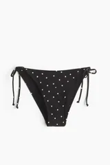 Bombacha de bikini vedetina negra con estampado de lunares blancos, tiro medio y tiras ajustables para atar en los laterales.