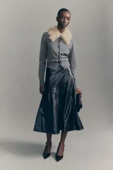 Cárdigan corto de punto fino color gris, con cuello desmontable de pelo sintético color beige. Presenta cierre frontal con botones y terminaciones acanaladas en puños y bajo.