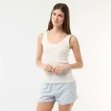 Conjunto de pijama de dos piezas compuesto por una musculosa blanca de tejido acanalado con detalles de encaje y un short celeste y blanco con estampado de cuadros vichy y terminaciones festoneadas.