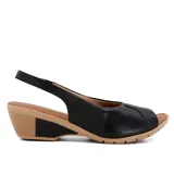 Sandalia de cuero negra con puntera abierta y talón cubierto. Cuenta con una tira trasera con hebilla y una plataforma de goma color beige con tecnología Care Juanetes.