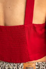 Top corto color rojo, con escote cuadrado y tirantes anchos. Presenta una hilera de botones marrones en el centro del frente.