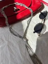 Collar tipo corbatín plateado con múltiples cadenas finas y cierre de mosquetón.