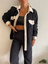 Camisa de pana negra con cuello, solapa, botones y bolsillos de parche en color crema. Corte recto y mangas largas.