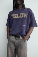 Remera de manga corta con corte relajado, confeccionada en tejido de algodón con textura tipo waffle. Presenta un efecto de lavado desgastado en color azul oscuro y estampado gráfico a contraste en el frente.