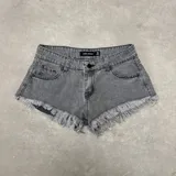 Short de denim gris oscuro de tiro medio, con bolsillos delanteros y traseros, cierre frontal con botón y bragueta, y terminaciones deshilachadas con flecos en el ruedo.