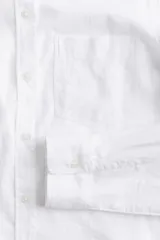 Camisa en tejido liviano de mezcla de lino y viscosa con cuello, botones adelante y canesú de doble capa con pliegue de caja en la espalda. Modelo de manga larga con bolsillo superior abierto, puños abotonados y bajo redondeado.