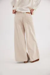 Pantalón sastrero de tiro medio confeccionado en pana de algodón. Presenta un diseño de pierna ancha con costuras verticales decorativas, bolsillos delanteros y traseros, y un detalle de aplique con ojalillo metálico en el ruedo de una de las piernas.