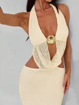 Vestido largo de tejido de punto color crema, con escote halter, abertura en la espalda y detalle de aro dorado en el centro del pecho.