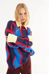 Sweater de punto con diseño geométrico en bloques de color azul marino, azul eléctrico y rojo. Presenta cuello polo en color amarillo y puños en el mismo tono, con un corte holgado y mangas largas.