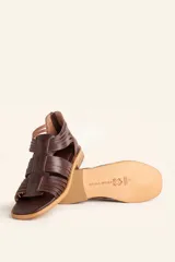 Sandalia de cuero color marrón chocolate, con suela plana y diseño calado con detalles trenzados.
