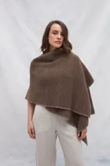 Ruana de tejido de punto industrial en color marrón, confeccionada en lana fina sin teñir. Presenta un diseño con doble ojal que permite mantener la prenda cruzada y cerrada.