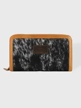 Billetera de cuero con paneles frontales de pelo vacuno con estampado animal print, ribetes de cuero marrón claro y cierre perimetral. Cuenta con un parche de cuero con logo grabado en el centro.
