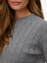 Sweater tejido de punto con cuello redondo y mangas largas con volumen. Presenta un diseño de tejido trenzado tipo cable y un calce regular.