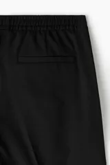Pantalón tipo jogger de vestir negro, corte slim fit, con pliegues frontales y traseros, cintura elástica con cordón de ajuste y bolsillos laterales y traseros.