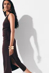 Vestido midi de punto color marrón, con diseño halter, escote pronunciado y frunces laterales que generan un efecto drapeado. Cuenta con cordón ajustable en la nuca adornado con cuentas en los extremos.