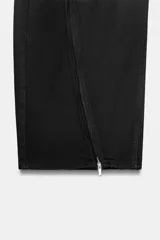 Jeans de corte baggy y tiro medio en color negro. Presenta diseño de cinco bolsillos y detalle de cremalleras verticales en el frente de las piernas con efecto torcido.